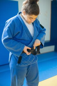 Woman in blue judo uniform adjusting black belt indoors. Martial arts focus.